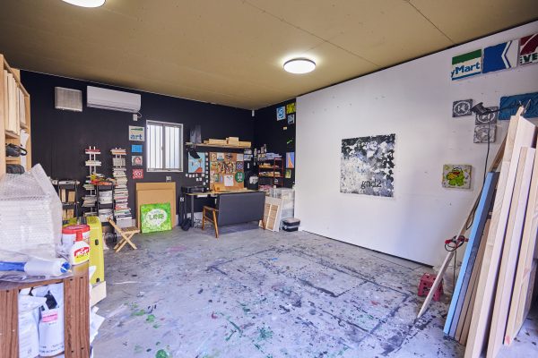 プレミアムガレージハウスに入居するアーティストさんのお宅。ガレージスペースを作品を制作するアトリエとして活用。壁に作品を掛けるためには釘を打つ必要があるため、柱を立てて、白く塗装した板を打ち付けてあるそう。